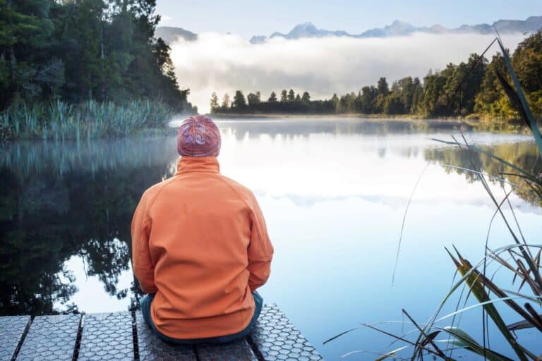 Man hiking in the New Zealand outdoors, resting by a lake.